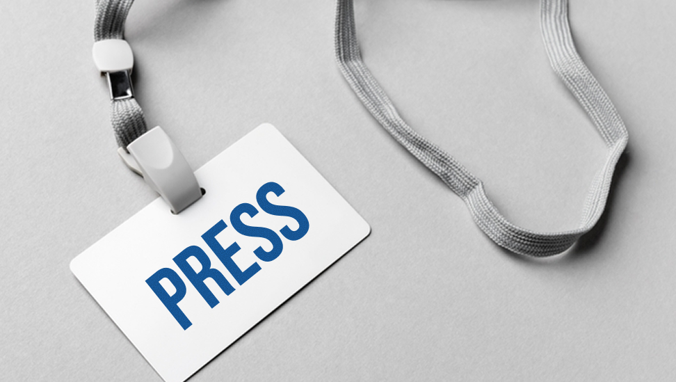 Press badge with grey lanyard on a neutral background