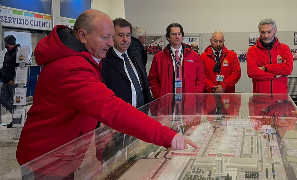 Person in a red jacket pointing at a section of the Hub model in front of a group of colleagues